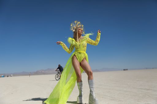 A woman in a neon yellow costume and a golden headdress poses in the vast, flat expanse of the Black Rock Desert during Burning Man 2019. In