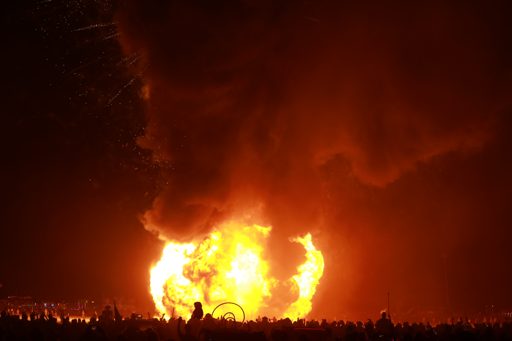 A massive explosion of fire and smoke erupts from the Man structure during the Burning Man 2019 "Man & Woman in Harness" event. A large crow