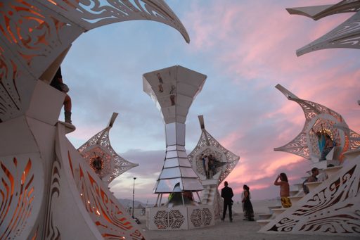 The "Temple of Transition" structure at Burning Man 2016, photographed at dusk with a pink and blue sky. The intricate white metalwork of th