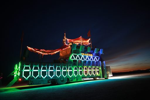 A large, illuminated art car, "The Dusty Rhino," is parked on the playa at Black Rock City, Nevada, during the annual Burning Man event. The