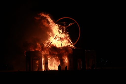 The Man, a large effigy, burns intensely at night during the Burning Man festival in Black Rock City, Nevada. The structure, featuring a cir