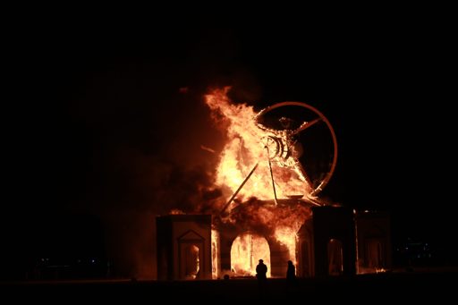The Man, a large effigy, burns brightly against the night sky at Burning Man 2016. The structure, featuring a circular wheel behind the figu