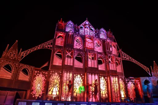 A temporary, Gothic-cathedral-inspired structure, illuminated with pink and purple lights, is seen at night during the Burning Man festival.
