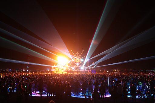 A massive crowd watches a laser light show at night during the Burning Man festival in Black Rock City, Nevada. The lasers emanate from a ce