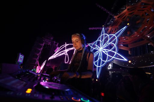 A female DJ performs at night on a stage adorned with a large, illuminated geometric star structure during the Burning Man festival in Lovel