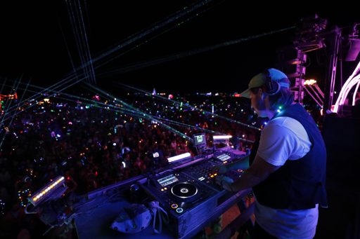 A DJ performs for a large crowd at night, illuminated by laser lights and glow sticks. The scene was captured during the "2017-08-29 · 100EO