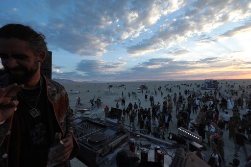 A DJ performs at dusk on the playa during the Burning Man festival in Lovelock, Nevada. The wide shot captures the vast desert landscape dot