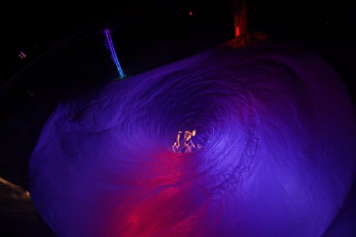 A swirling vortex of purple and pink light illuminates a group of people in the distance at the "Lovelock" art installation during Burning M