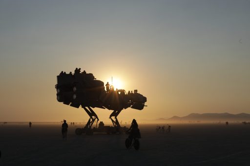 A large, mechanical, dinosaur-like art installation, "The Great Art", is silhouetted against the setting sun at Burning Man in Lovelock, Nev