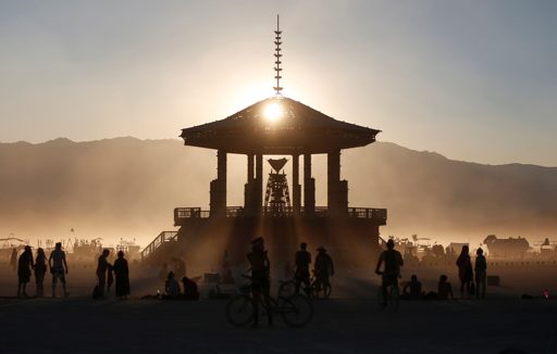 Silhouettes of people and bicycles gather near the Temple structure at sunset during Burning Man 2017 in the Black Rock Desert, Nevada. The