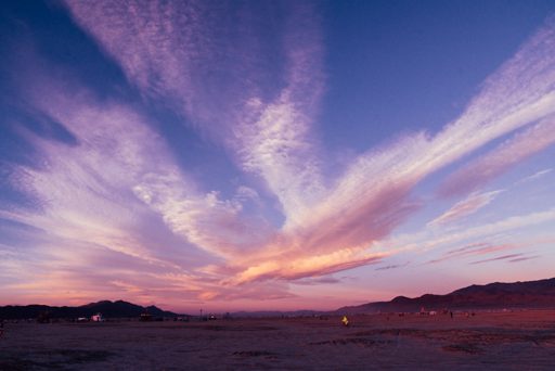 A dramatic sunset sky with wispy clouds painted in shades of pink and purple over the Black Rock Desert, Nevada, during Burning Man. The vas