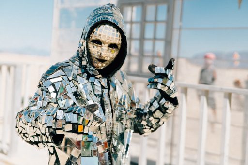 A person in a mirrored costume and mask poses outdoors during Burning Man 2015. The costume is made of numerous small, reflective square and