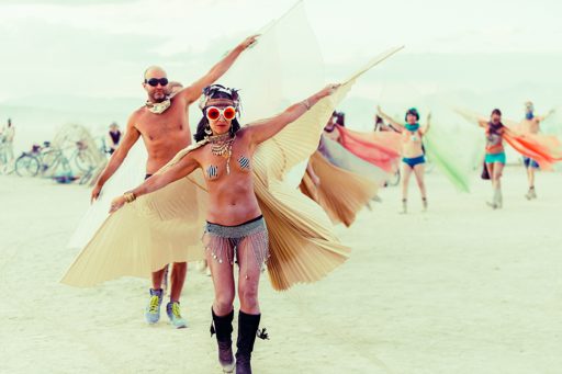 Two participants in elaborate costumes, one with large golden wings and the other with white wings, dance during the Burning Man festival in
