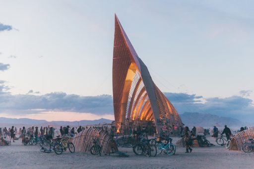 The "What Lies Beneath" pavilion, an art installation at Burning Man 2015, is illuminated at dusk. The structure, made of wood and metal, fe