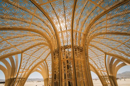 The intricate, geometric golden canopy of the "Temple" structure at Burning Man 2015, photographed from below against a clear blue sky.