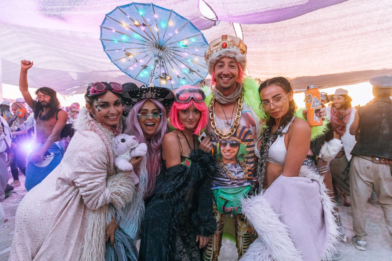 A vibrant group of five people in elaborate, colorful costumes pose joyfully at a lively outdoor festival.