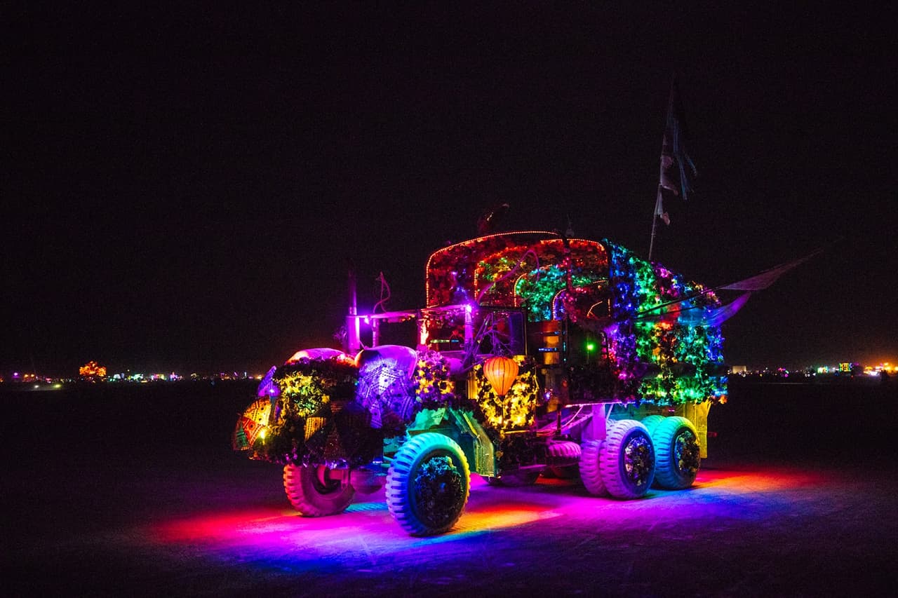 A vibrantly illuminated art car glows with a multitude of colorful lights in the dark desert night.