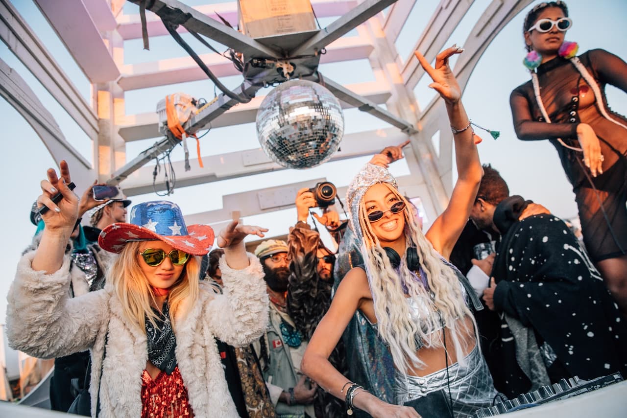 Two women in festive attire dance energetically at an outdoor party under a disco ball.