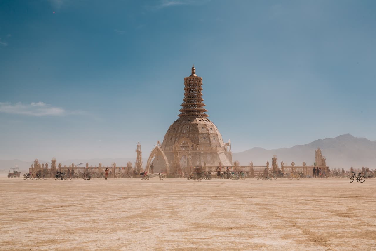 A grand, ornate temple-like structure stands majestically in a vast, flat desert under a clear blue sky.