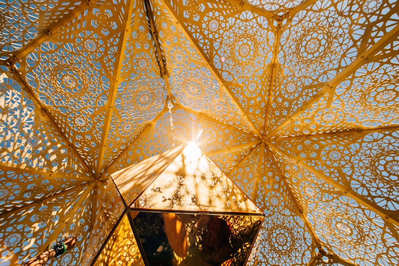 A dazzling golden geometric art installation features intricate patterns and a central light source shining brightly.