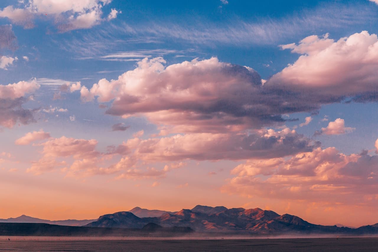 A breathtaking desert landscape at sunset, featuring a vast expanse of flat land under a sky filled with dramatic, colorful clouds.